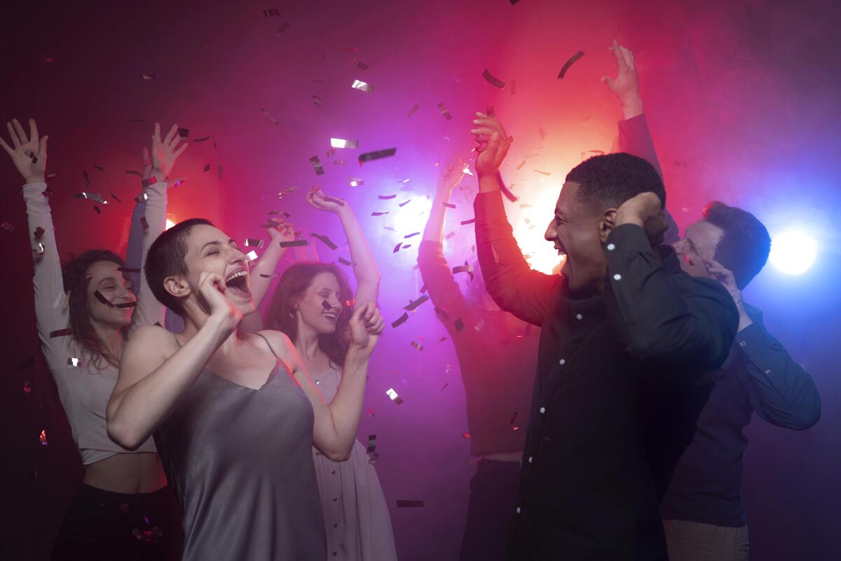 Grupo de amigos dançando sob iluminação quente e colorida em uma festa animada