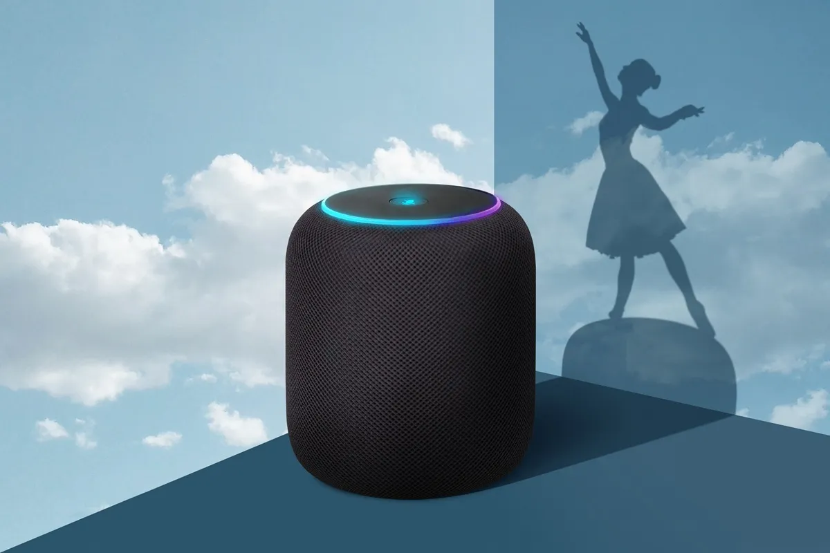 Caixa de som inteligente preta com luz LED colorida no topo, projetando a sombra de uma bailarina contra um fundo de céu azul com nuvens.