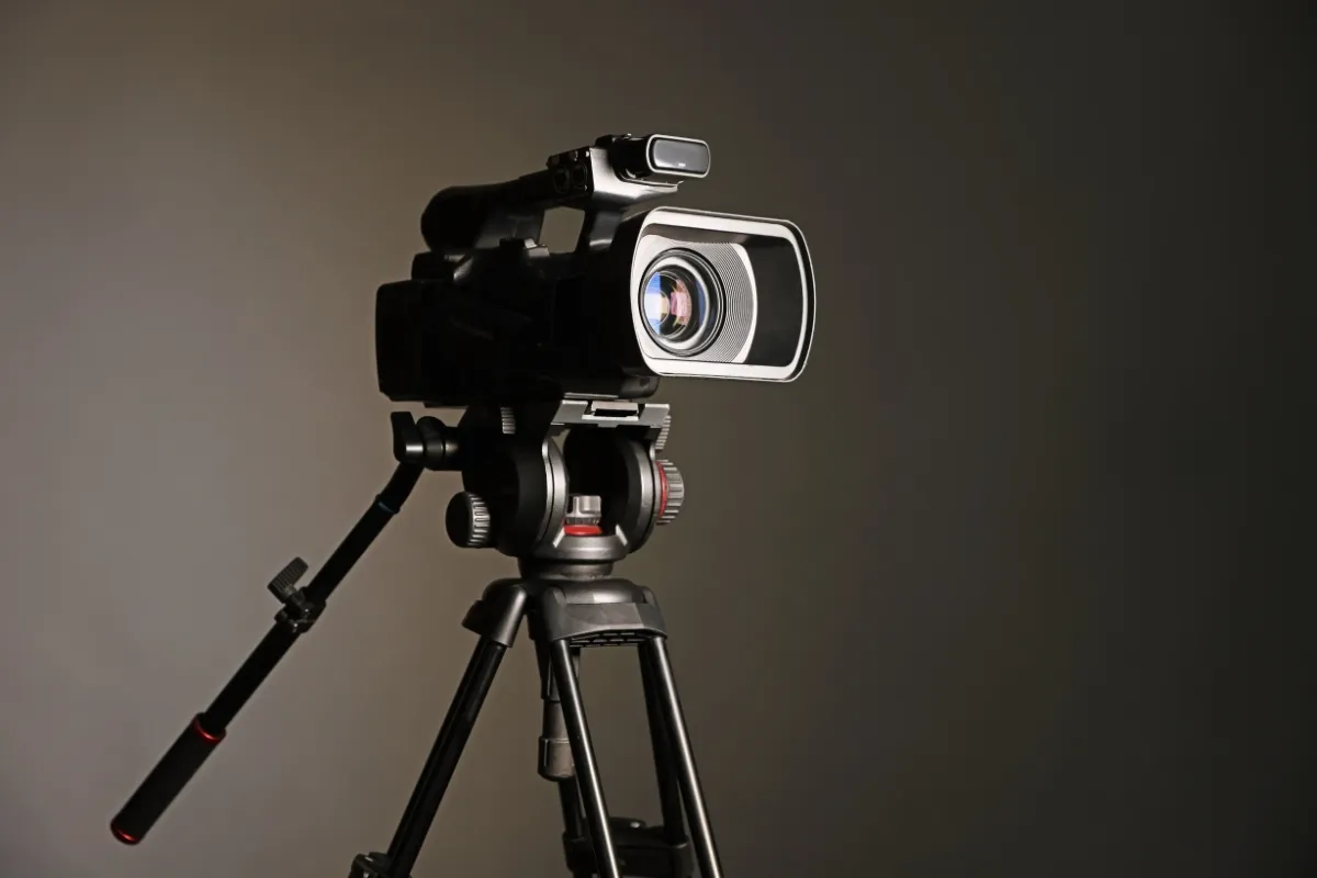Câmera de filmagem montada em tripé com lente frontal em destaque sobre fundo neutro
