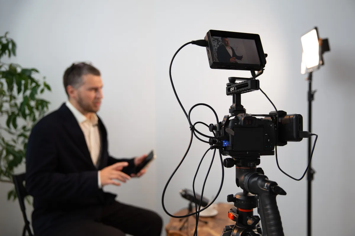 Câmera profissional montada em tripé gravando um homem sentado que fala diante de uma luz de estúdio.